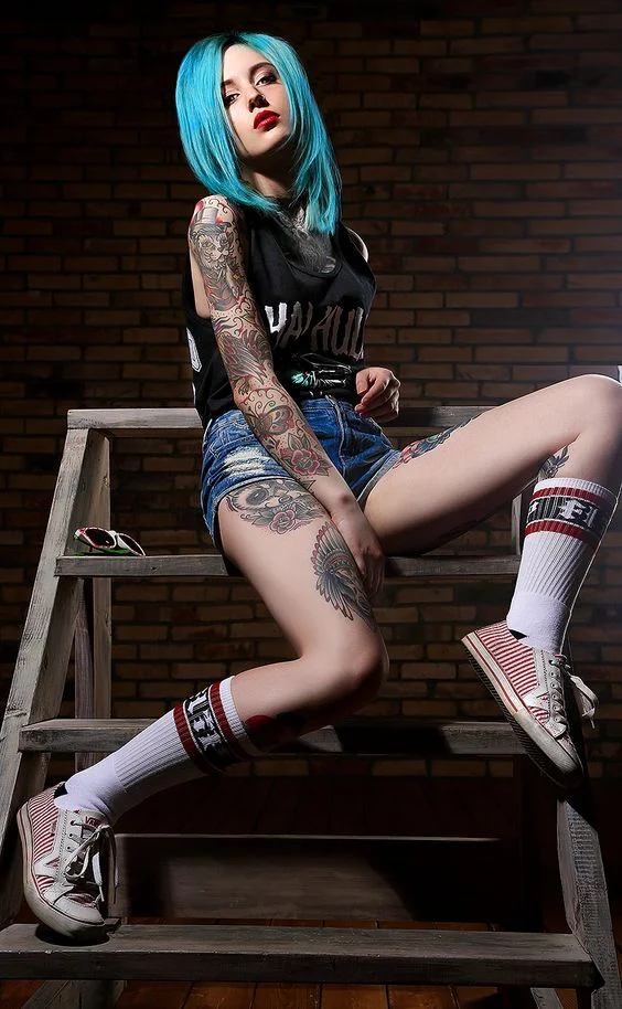 Foto de una chica sentada relajadamente con deportivas, lleva tatuajes estilo old school en piernas