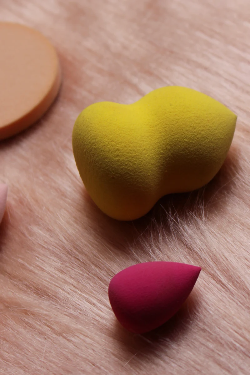 a close-up flatlay of various makeup sponges on a rose-gold background