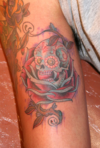 This is a very vivid red rose body tattoo with a black stem and large text