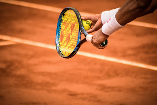 Photo of a man serving a tennis ball on a clay court.