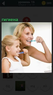 Перед зеркалом в ванной чистят зубы мать и ребенок, соблюдая гигиену
