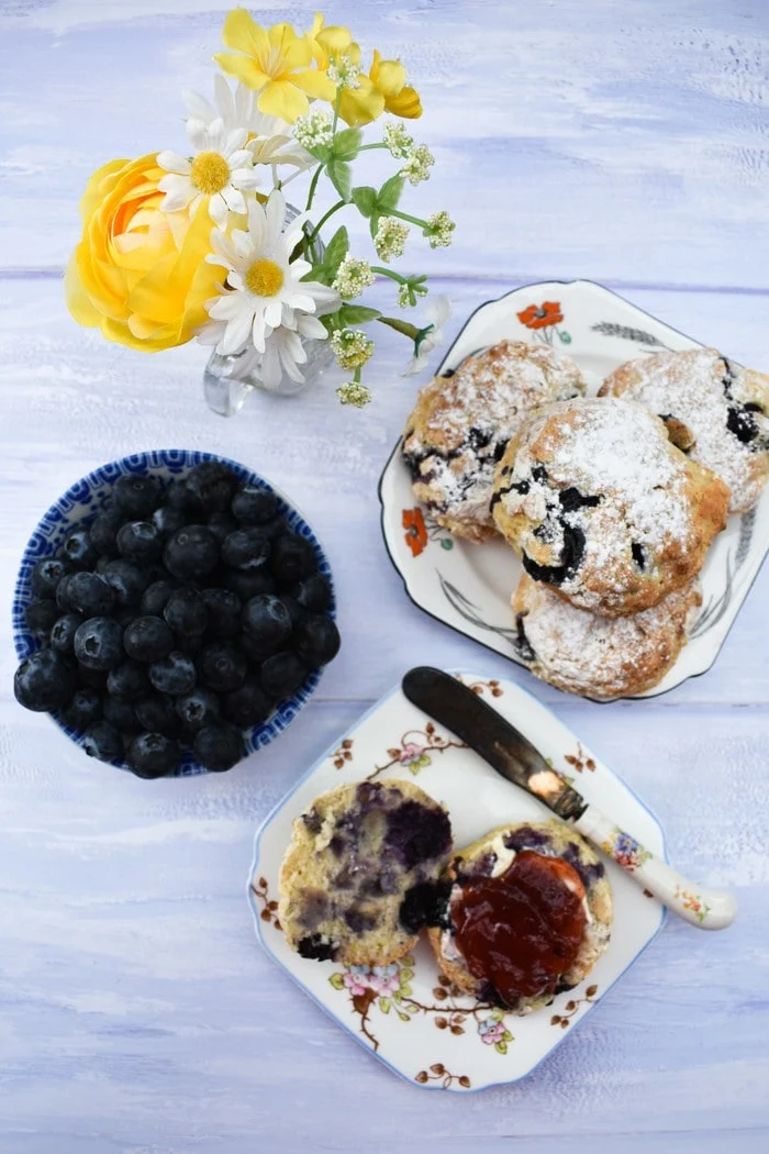 Overhead view of Blueberry Lemonade Scones, a bowl of blueberries and jar of  flowers