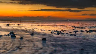 4K image of a dramatic sunset over a low tide sea with scattered rocks and reflective water.