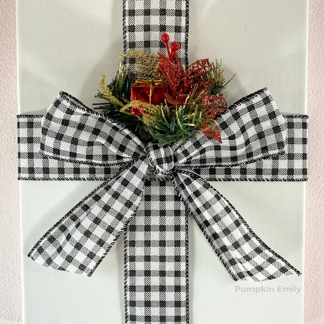 A close up of a flower pick and plaid ribbon on a canvas that looks like a present.