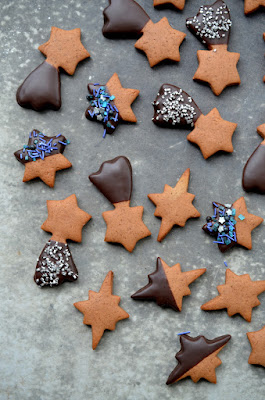 Lebkuchen in verschiedenen Sternformen liegen auf einem dunklen Hintergrund, der ein wenig nach Sternenhimmel aussieht. Die Lebkuchen sind mit Schokolade und Zuckerstreuseln in Silber und Blautönen verziert.