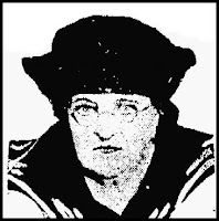 A poor quality picture of a white woman of late middle age, with sharp features, wearing round spectacles and a sailor-style blouse and hat