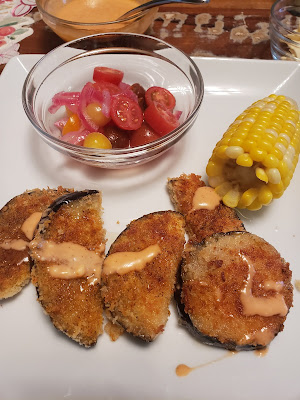 a plate of spiced, fried eggplant, corn on the cob, and tomato salad