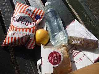 A bag of popcorn, a bottle of water, an apple, a brownie bar and a sandwich wrap.