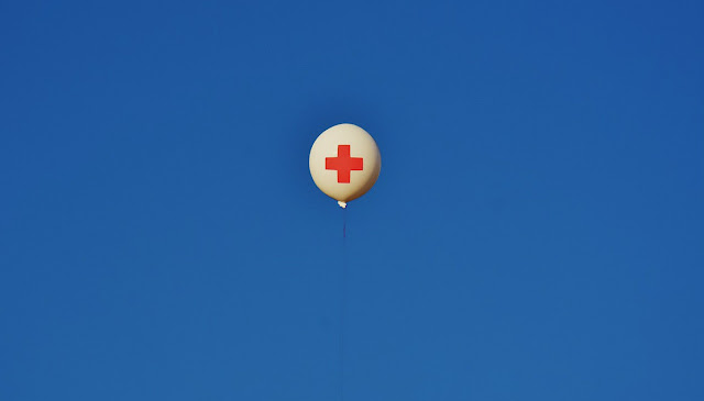 White balloon emblazoned with a red First Aid cross floating against a bright blue sky