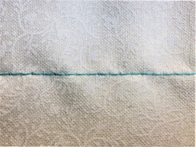 Blue thread on white fabric shows uneven stitchin