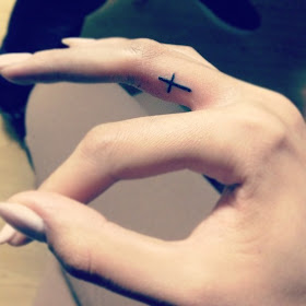 Simple cross tattoo on middle finger