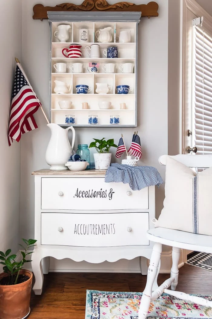 wall cubby hung above small dresser, filled with vintage red white and blue creamers and flags
