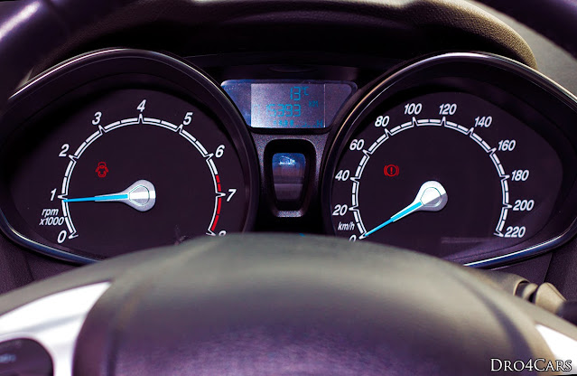 The instrument cluster of the 2014 Ford Fiesta (six-gen). Black background, white letters with the red zone on the rpm and nice blue arrows.