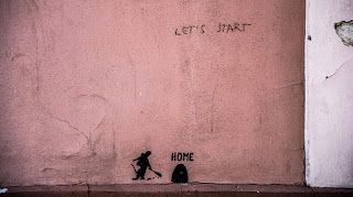 Graffiti Text "Let's Start" oben, unten am Boden ein kleines schwarzes Mauseloch überschrieben mit "Home", jemand ist gerade dabei zu schaufeln