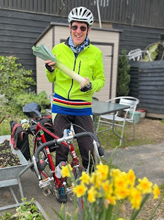 daffodils in foreground, cyclist in yellow jacket holding large leek