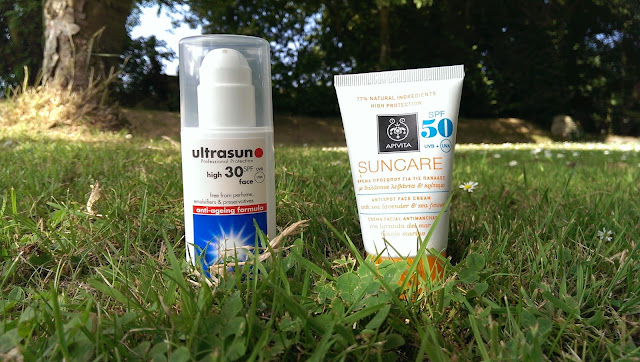 A picture of Ultrasun and Apivita sun protection sitting in the grass on a sunny day