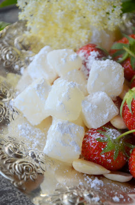 Holunderblütenkonfekt liegt zusammen mit frischen Erdbeeren und einigen Mandeln auf einem silbernen Teller.