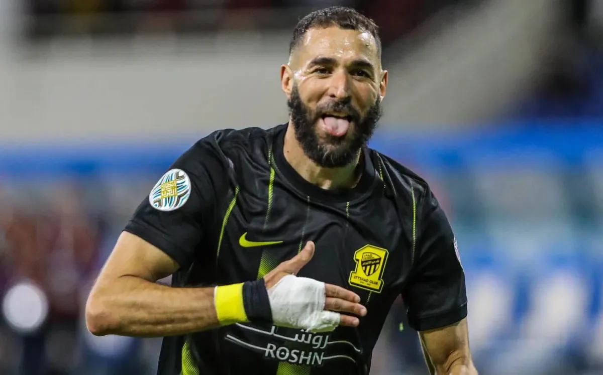 karim benzema comemorando um gol com expressão de alegria e fazendo sinal de coração na camisa do al hilal em campo.