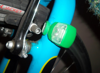 Bike light in green clamp wrapped around front-left fork of bicycle near wheel rim