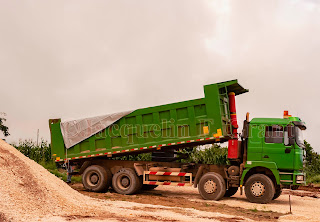 A green tipper body truck is parked beside a load of marl on a road construction sight on a cloudy day.