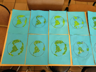 Prace plastyczne wykonane na zajęciach przez przedszkolaków leżą obok siebie na stoliku. Prace przedstawiają zielony kontynent Ameryki Północnej i Południowej na niebieskim tle.