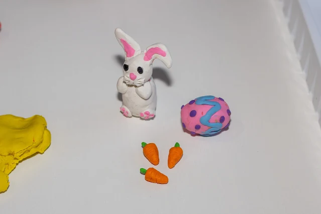 Plasticine white Easter bunny, some small orange carrots and a patterned Plasticine Easter egg