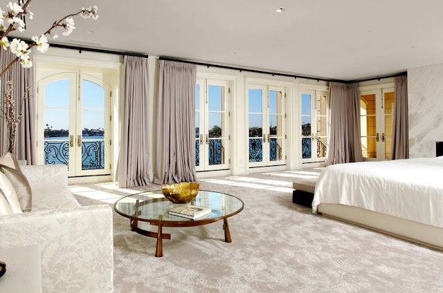 master bedroom with an ocean view,  floor length light purple curtains, french doors, a round glass table, a white sofa and a white bed