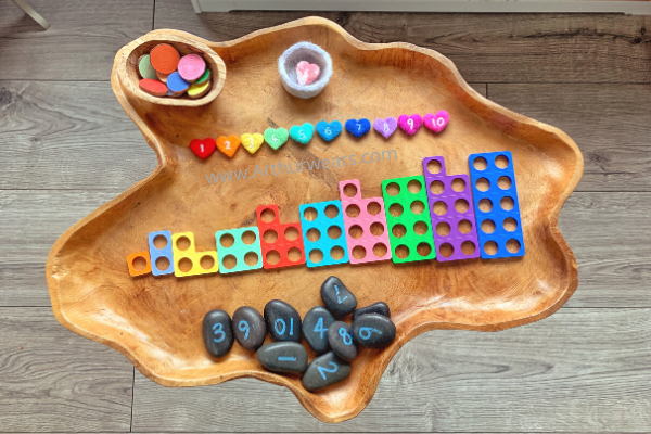 needle felt rainbow hearts with numbers to ten on a wooden tuff tray with numicon, number stones, rainbow wooden discs and loose parts