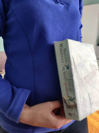 Czytelniczka w granatowej bluzie polarowej prezentuje książkę pod tytułem Jeszcze się kiedyś spotkamy Magdaleny Witkiewicz.