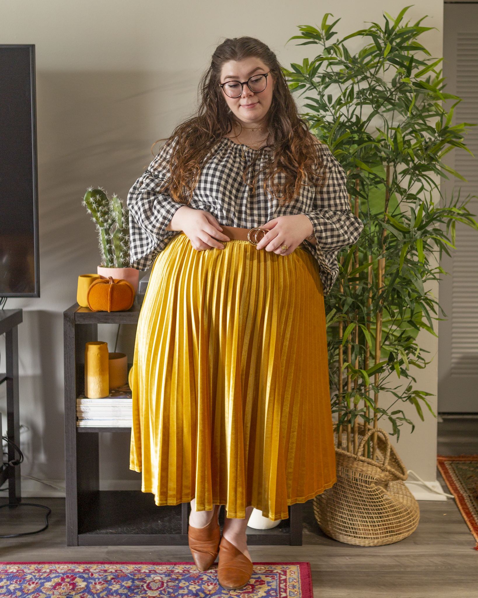 An outfit consisting of a black on white off the shoulder with bell sleeves tucked into a mustard yellow velvet midi skirt and brown d'orsay flats.