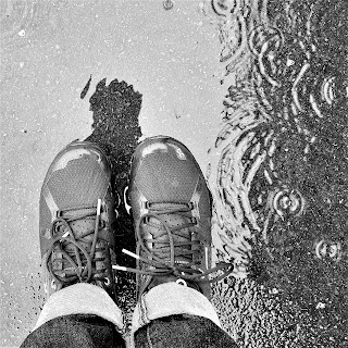 Photo looking down at walking shoes in a puddle in the rain