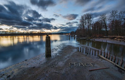 The word "Peace" spelled out with rocks close to water.