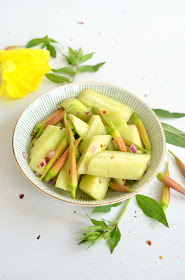 Salat aus Gurken und Chili mit Knospen der Nachtkerze. Der Salat ist in einer hellen Schüssel angerichtet, rundherum liegen Blätter, Knospen und Blüten der Nachtkerze.