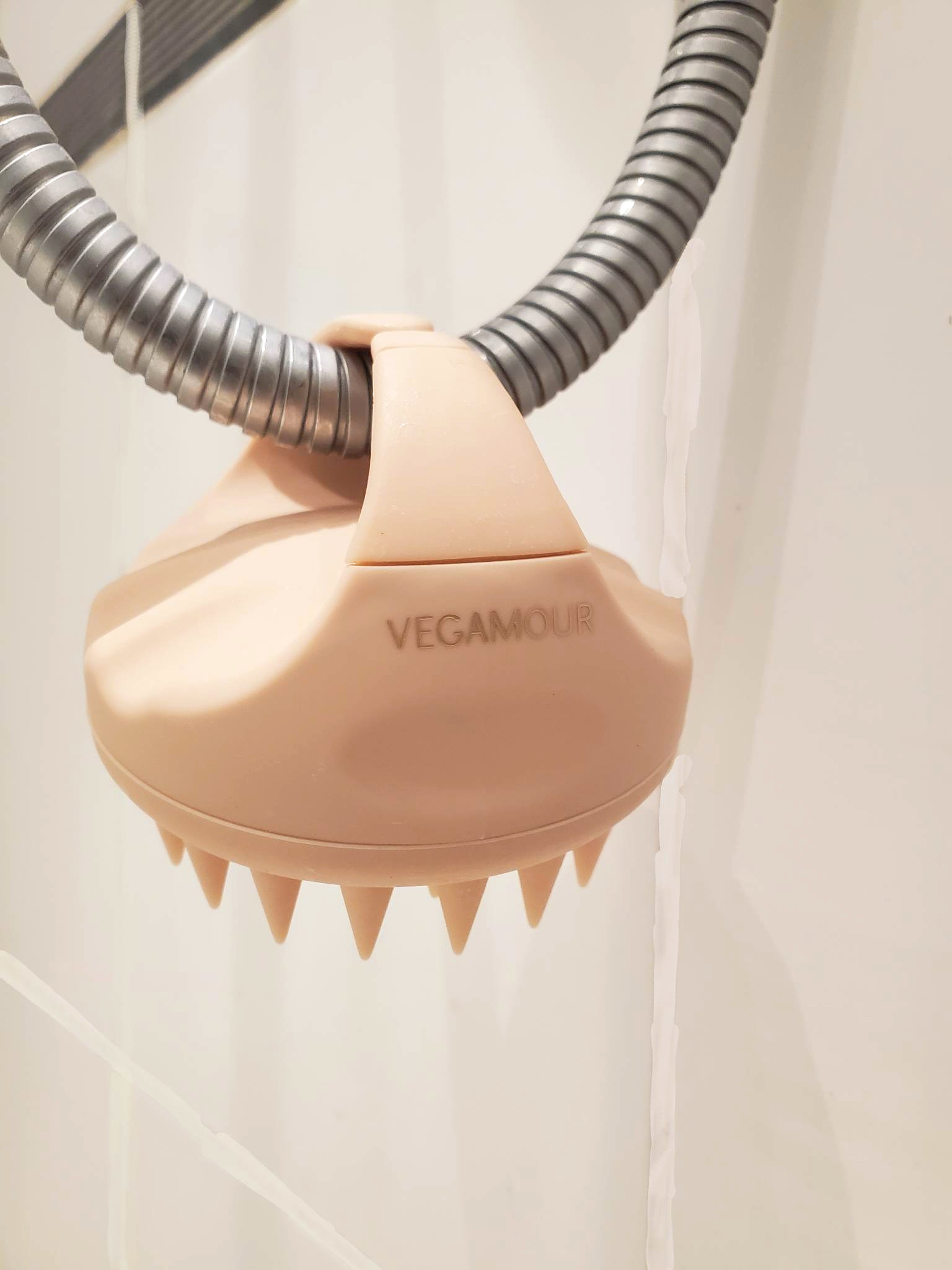 Vegamour Gro Scalp Revitalizing Massager in pastel pink hanging from shower