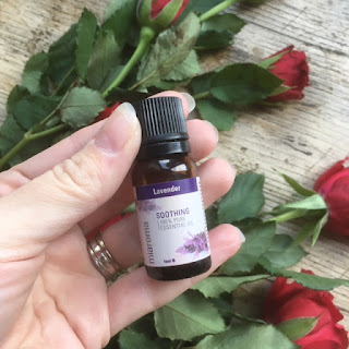 Woman's hand holding a purple bottle of lavender essential oil to a backdrop of red roses