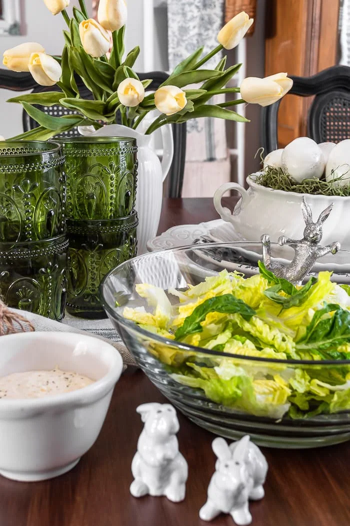 Caesar salad dressing, glass bunny bowl of lettuce, stacks of white dishes, green glasses, white tulips