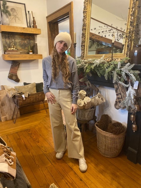 standing in a pants in cream with a cream beanie and gray sweater