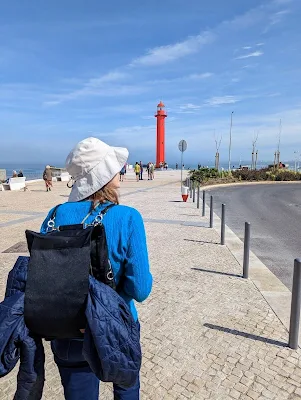View of the author from behind. She is wearing a Driibe backpack with her jacket tucked into the rear slot. A bright red lighthouse is in the distance