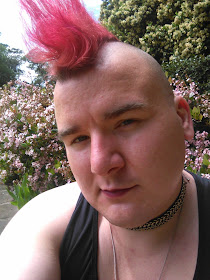 A person in a black tank top and a chain choker with a pink mohawk.