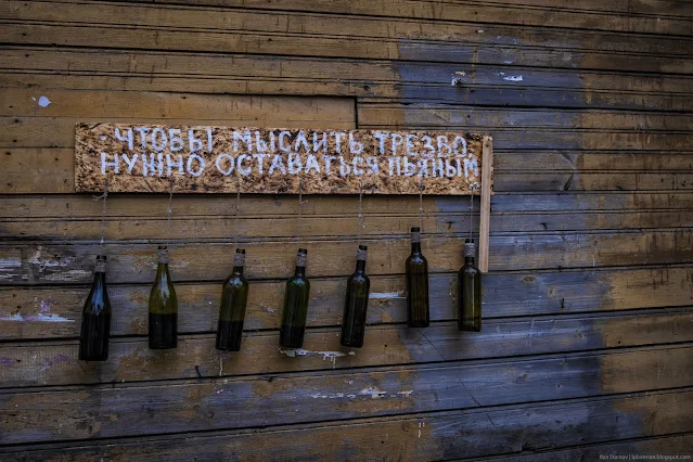 Бутылки развешаны на стене с надписью Чтобы мыслить трезво нужно оставаться пьяным