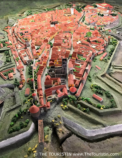 The red rooftops and two white church towers of a medieval miniature town model.