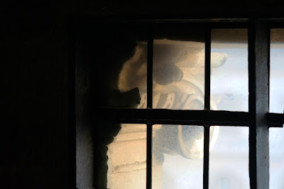 A stone column capital seen through a small-paned window.