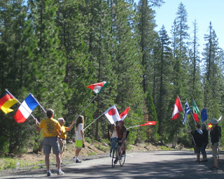 Cyclist pedals through volunteers waving international flags at the Gumboot water stop, W A Barr Road, Mt. Shasta, California