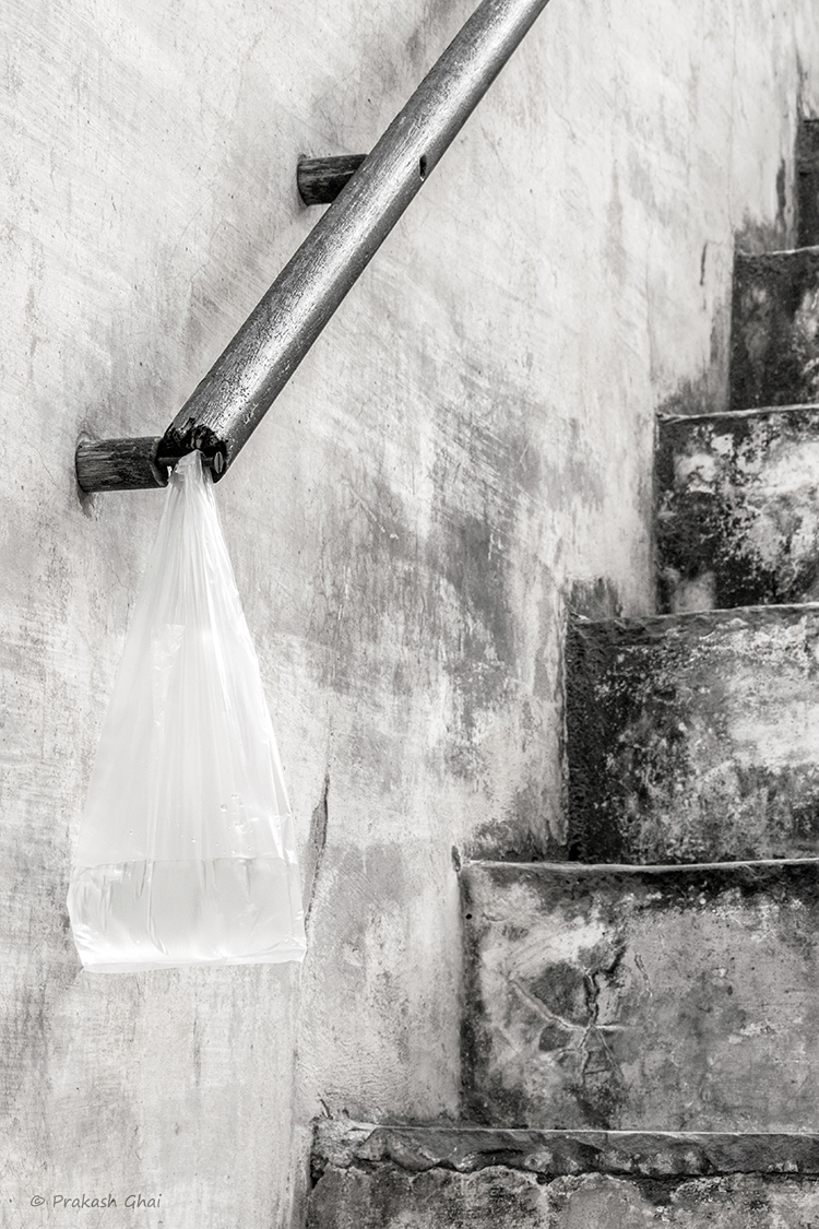 A minimalist photo of A plastic bag containing water, hung on the railing of a staircase.