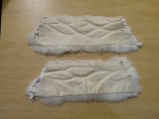 Trapezoidal-shaped 1850s fur cuffs, lying with the white fur facing down and the polished-cotton lining facing up.