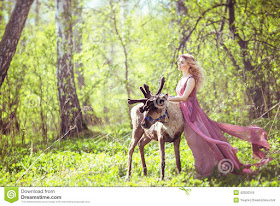 Girl in fairy dress with a flowing train on the dress and reindeer in the forest