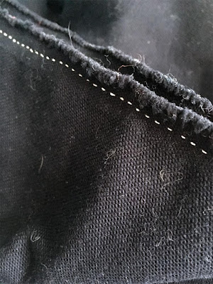 A close-up of a neat backstitched seam in white thread on blue-black fabric with very fuzzy edges in the seam allowance.