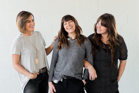 Three smiling young women representing a polyamorous triad/throuple