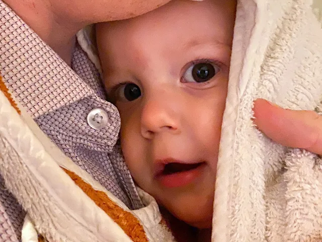 baby boy on his first birthday in an apron towel being cuddled up to his father's chest