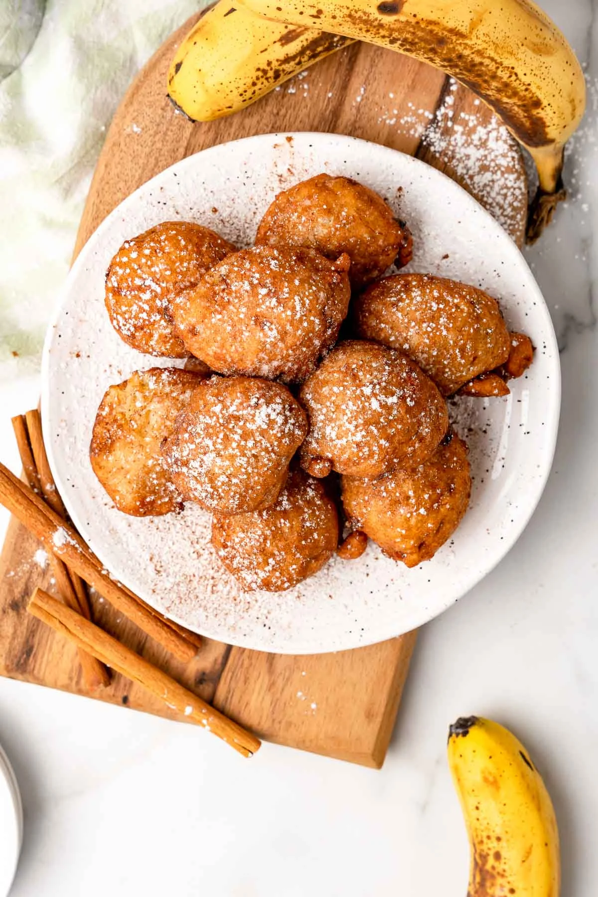 Fried banana fritters on a white plate with dusting of powdered sugar and cinnamon.